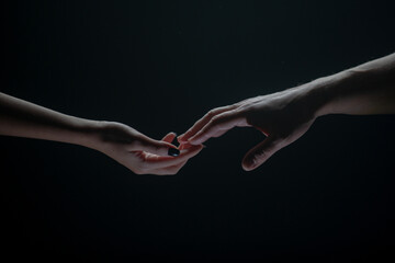 Two hands stretch each other, black background. Couple in love holding hads, close up. Helping...