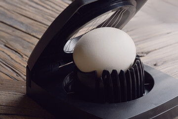 Hard boiled Egg in an Egg Slicer tool, on an old rustic table. Macro photo with shallow depth of...