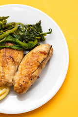 Grilled caviar cod fish with greens and fresh lemon on white small plate.