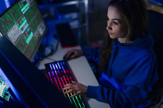 Young woman hacker by computer in the dark room at night, cyberwar concept.