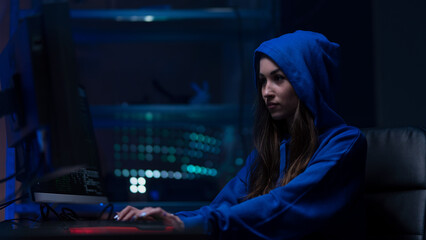 Young woman hacker by computer in the dark room at night, cyberwar concept.