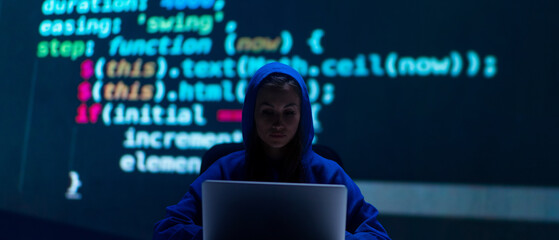 Hooded anonymous hacker woman by computer in the dark room at night, cyberwar concept.