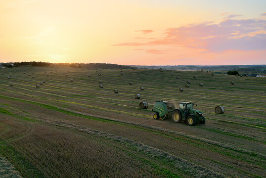 John Deere Tractor 6715R with John Deere V461R round baler making Hay Bales in an agricultural field. Farm Round Hay Bale Tractor Baler. Balers to roll. Russia, Smolensk, September 13, 2021.