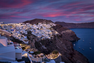 Panoramic view of the illuminated village Oia at the edge of the caldera, Santorini, Greece, during dusk