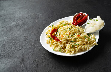 Instant noodles in a white plate on a black background - top view. National fast food. Quick lunch