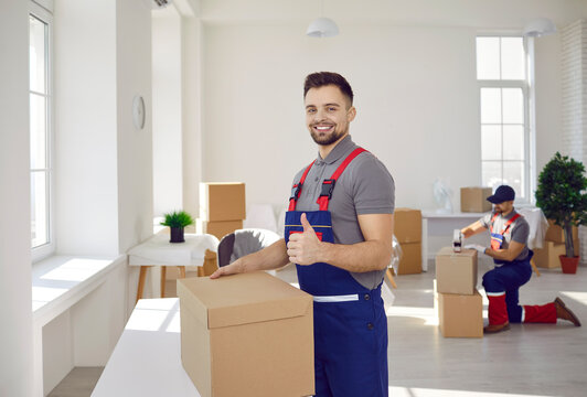 Happy male mover worker with cardboard box show thumbs up recommend good quality delivery company service. Smiling deliveryman with package give recommendation to moving or relocation help.