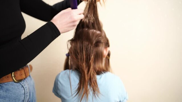 Mom combs her daughter's wet hair before cutting and collects in the tail. cutting hair at home. life hacks and rules of hair care. special combs and scissors for hairdressers.