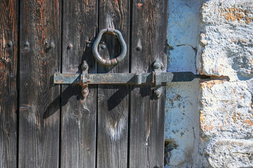 An old wrought iron door knocker, a metal latch and a lock on an old wooden door in the Russian style.  The forged hammer handle and the handmade latch are made of iron close-up against the background