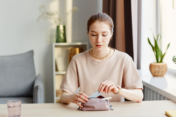 Minimal portrait of young woman putting birth control pills in cosmetic bag with other feminine...