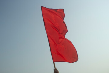 Red flag in his hand against sky. Red matter on pole. Signal to start start.
