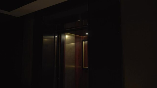 Smooth opening of the empty elevator doors in dark lobby. Elevator cabin with light in brown shades with mirror. Easy movement through the floors in a hotel, residential building, office building.