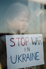 Child at the window and calls No War. Poor girl protesting war conflict raises banner with...