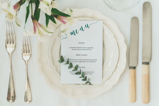 Flat lay shot of wedding or party place setting. Formal dining concept image with crockery, plates, menu and flower arrangements in shot.