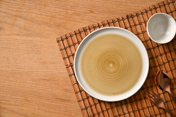Mockup of empty ceramic plate, bowl and silverware on bamboo place mat