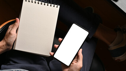 Male hands holding empty spiral notepad and cellphone mockup