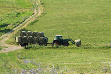 Obraz premium Tractor driving hay fresh bale on the field.