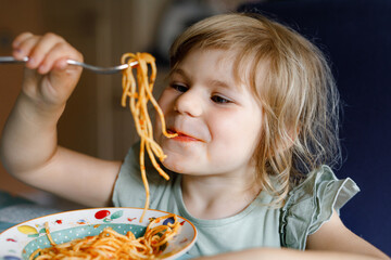 Adorable toddler girl eat pasta spaghetti with tomato bolognese with minced meat. Happy preschool...