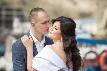 a guy in a suit and a girl in a white dress are standing and hugging..