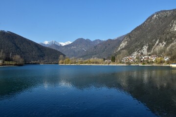 View of lake at Most na Soci and Modrej village with snow covered mountain peak of Julian alps behind in Severna Primorska, Slovenia