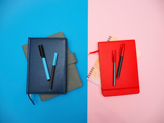 top view flat lay of blue and red notebooks and pens on blue-pink background.