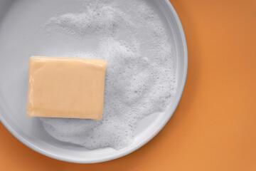 Top down view mockup peach pastel orange color vitamin c soap bar square shape with foam bubbles water on white plate and solid plain orange as background