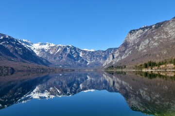 Snow covered mountain peaks in Julian alps and lake Bohinj with the reflection of the mountains in the lake in Gorenjska, Slovenia