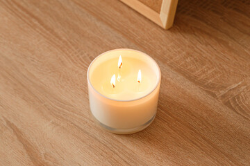 Fototapeta na wymiar A large scented candle with three burning wicks and melting wax in a glass standing on a wooden table. Side view. Place to copy