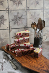 Chocolate brownie with cherries and cheese layer. Many pieces of chocolate dessert with berries on a wooden board	