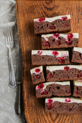 Chocolate brownie with cherries and cheese layer. Many pieces of chocolate dessert with berries on a wooden board	