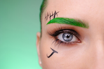 Woman with creative joker  clown makeup. Trendy halloween green carnival costume. Eye close-up...