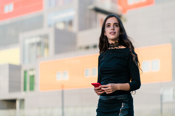 Young woman standing holding her phone as she looks away in city