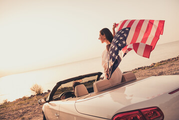 Photo of funny carefree married couple dressed white clothes driving car holding american flag outdoors country side road - obrazy, fototapety, plakaty