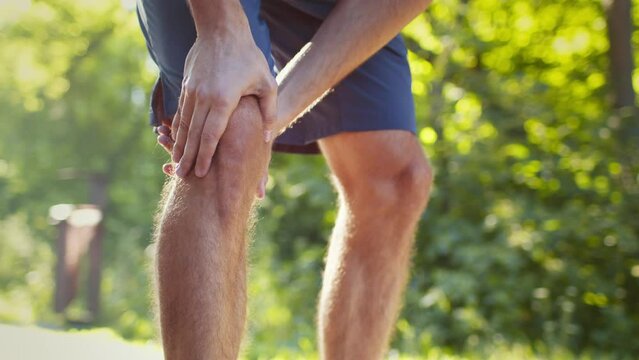 Unrecognizable man jogger running and feeling acute pain in knee, massaging leg during morning run in park, free space