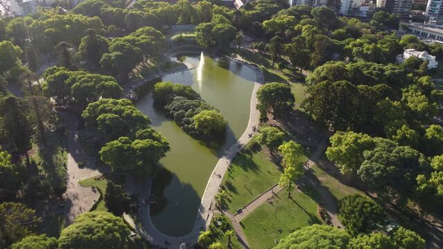 Aerial birds eye shot of Centenario Park in Buenos Aires during sunny day with green trees,lake and walking people