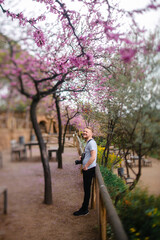 Fototapeta premium Man with camera leaning on fence at blossoming park in Spain