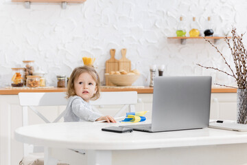 Little beautiful girl study at home while quarantine. Cute child doing homework online sitting in the kitchen . The concept of learning at home for schoolchildren. Distant study concept
