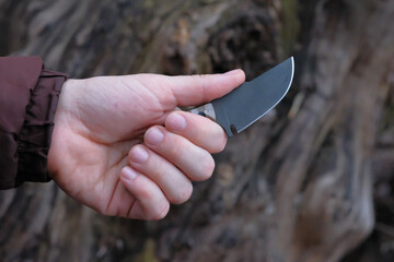 - Exclusive handmade knife in hands of man on background of big tree.
