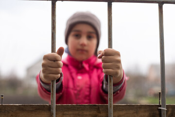 Little girl behind bars. Concept of homeless children. Child captivity. Sad child