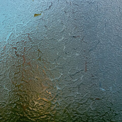 Frozen glass with the onset of cold weather. View through a layer of ice to the blue sky. Frost on the windshield, the rays of the morning sun melt the frost formed overnight. Background, texture.