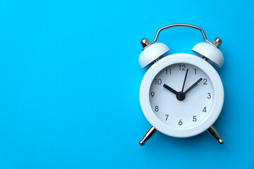 White analog alarm clock isolated on blue background. Concept of time management or business. Copy space. Close-up.