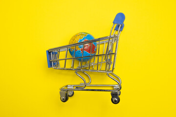 Mini shopping trolley cart with globe on yellow background. World globe in the mini cart, international trade around the world concept. 