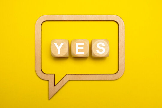 Wooden speech bubble concept with inscription YES isolated on yellow paper background with drop shadow. Copy space.