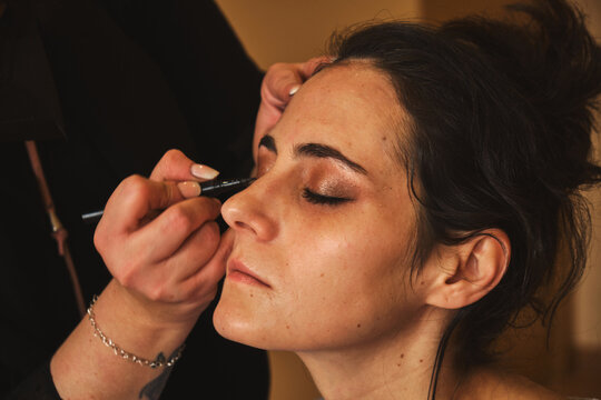 Young caucasian dark-haired woman with her eyes closed getting her makeup done in a room