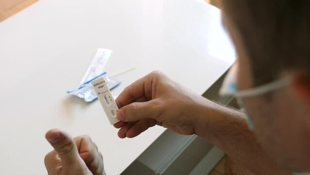 Adult male hold fast coronavirus atk with 1 stripe, not infected, takes off his face mask. Man check result of covid-19 rapid antigen test kit he did self at home, negative, recovered, man is happy.