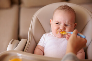 Baby making funny faces while refusing to eat porridge - obrazy, fototapety, plakaty