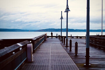 Man stands on the end of a dock on Ruston Way in Tacoma WA looking out at the water