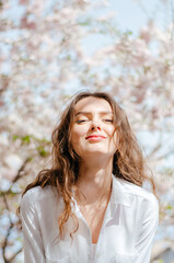 Naklejka premium young girl in a white shirt is photographed near the blossoming sakura in the spring