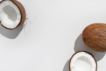 Fresh whole and broken pieces tropical coconut nut with sunny contrast shadows on light gray background flat lay top view. Creative summer food background, exotic organic healthy diet fruit