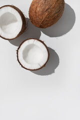 Fototapeta na wymiar Fresh whole and broken pieces tropical coconut nut with sunny contrast shadows on light gray background flat lay top view. Creative summer food background, exotic organic healthy diet fruit