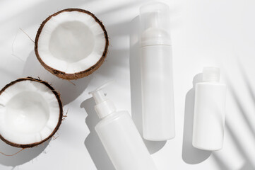 White cosmetic bottles broken fresh coconut with sunny contrast shadows palm leaf on gray background. Organic natural cosmetics with coconut oil. Plastic packaging products for branding, mock up